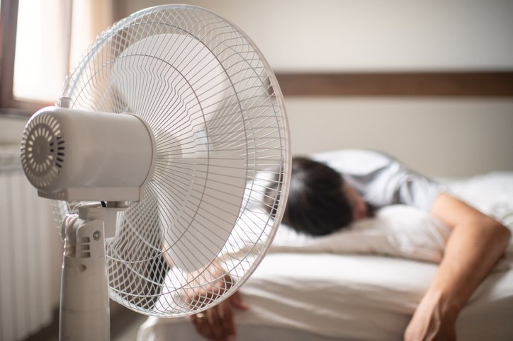 Hombre durmiendo junto a un ventilador sin el mejor colchón para calor