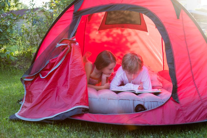 Niños leyendo sobre un colchón hinchable dentro de una tienda de campaña