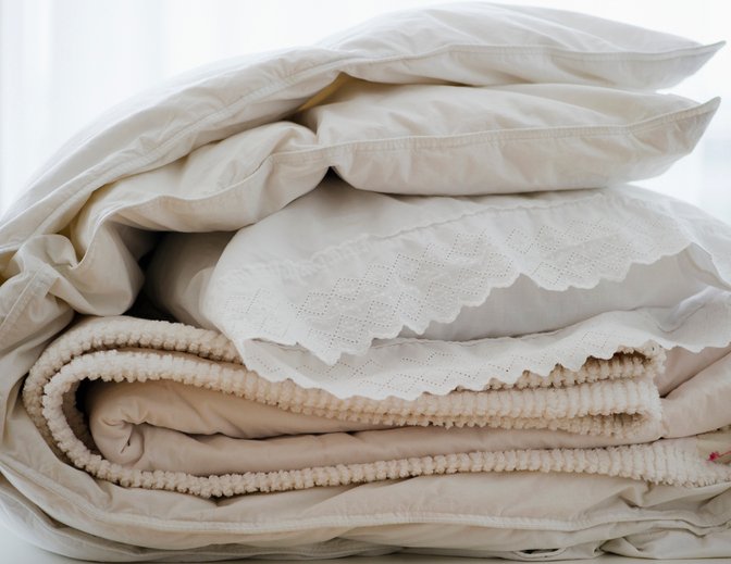 Ropa de cama doblada junto a un protector de colchón